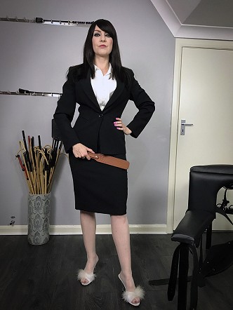 Miss Jessica in her office wear, high heeled fluffy slippers holding a brown leather paddle